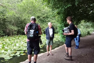 People standing by pond with lily pads for our Welsh wildlife walk at Forest Farm.