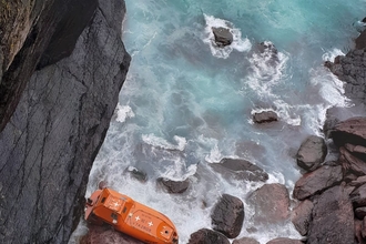 An orange lifeboat run aground on rocks below Skokholm Island.