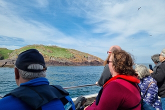 A group of people on a boat looking out to Skomer Island on a bright sunny day. 