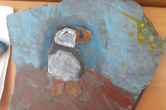 Puffin painted on slate with sky and rocks in background