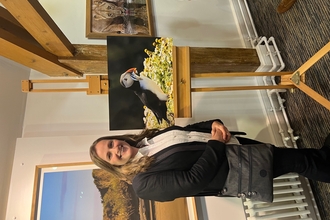 Sarah stood next to a photo of a Puffin in a gallery. 