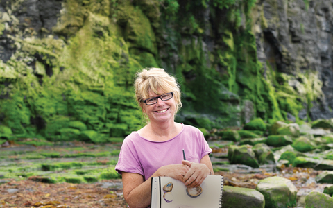 Carol sits on the beach with her sketchbook