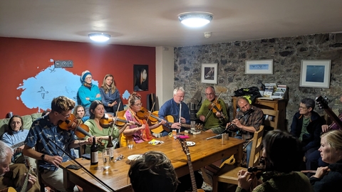 A group of musicians playing music in the hostel lounge. It is crowded and all are playing.