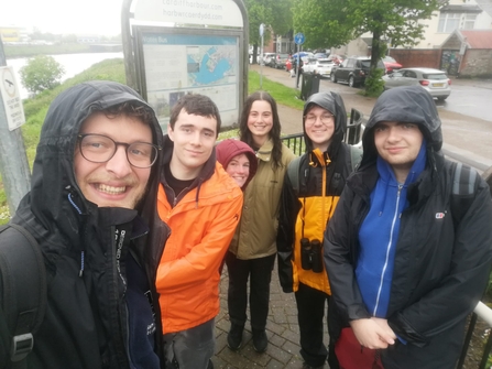 A group of people take a selfie next to the river, all soaking wet from the rain!