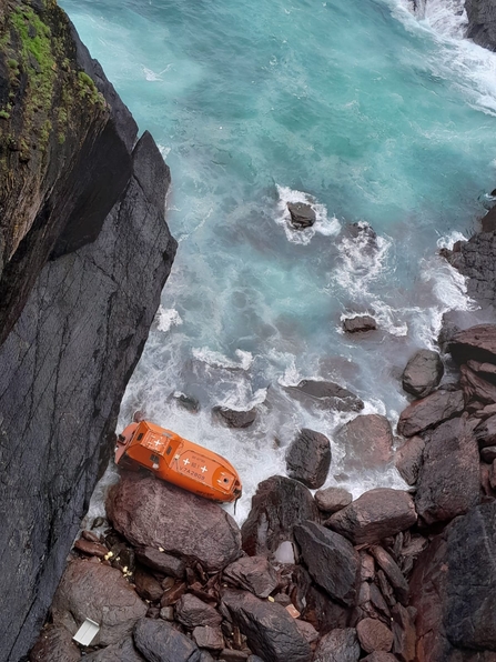 An orange lifeboat run aground on rocks below Skokholm Island.