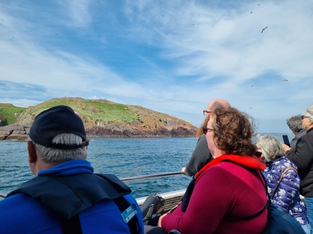 A group of people on a boat looking out to Skomer Island on a bright sunny day. 